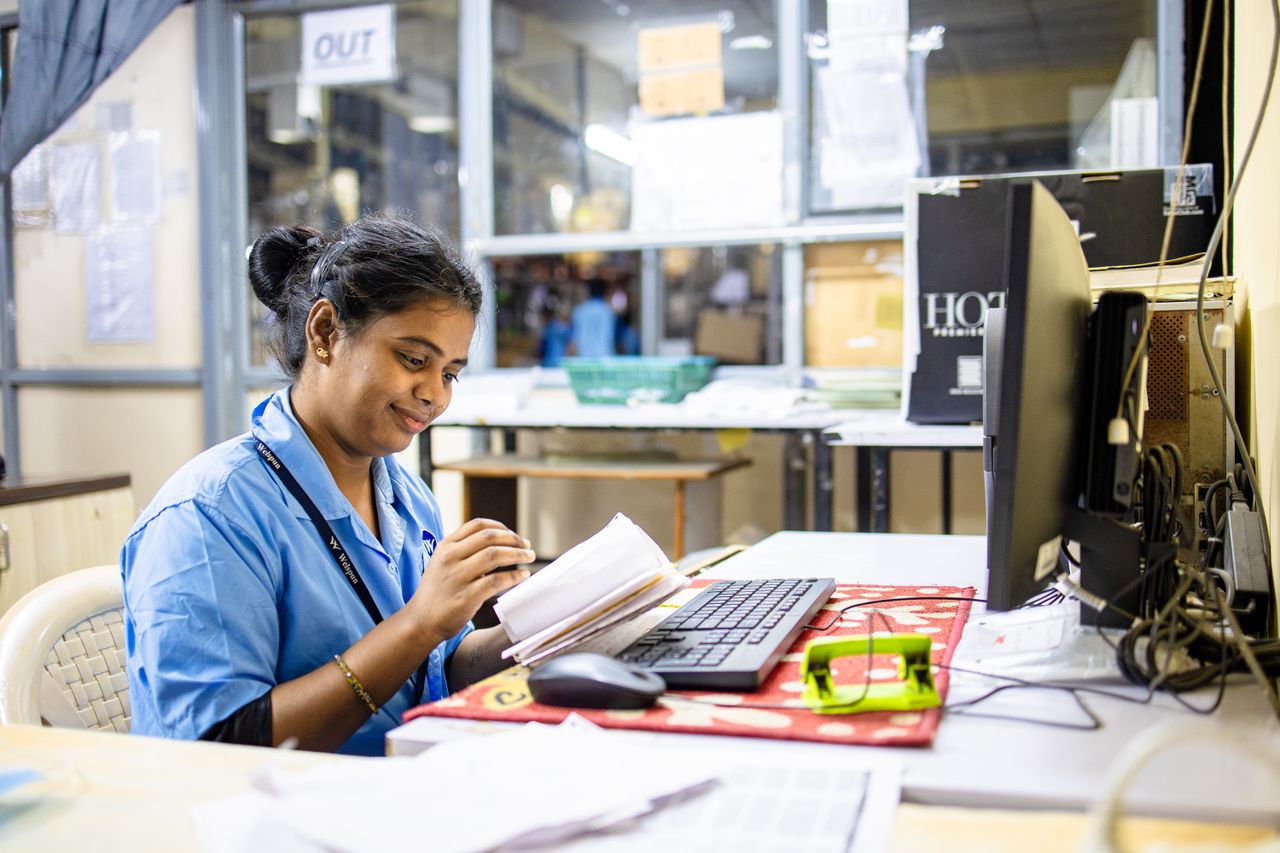 Smiling woman in blue uniform working at office desk with computer and paperwork.