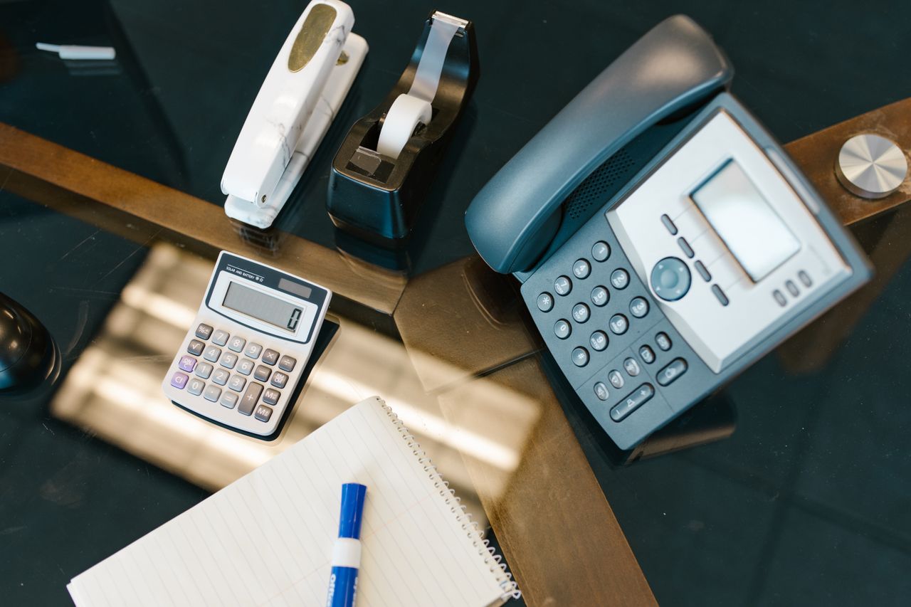 A neatly arranged office desk with a calculator, phone, stapler, tape, and notepad.